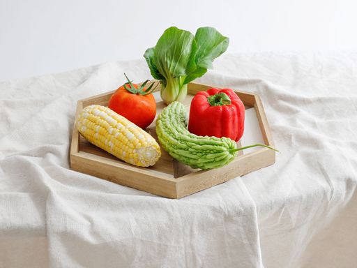 A wooden board with tomato, pepper, bitter gourd, corn and lettuce on white background