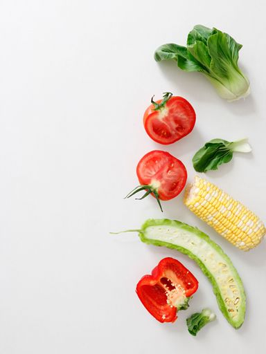A top view of cut tomato, pepper, bitter gourd, corn and lettuce on white background