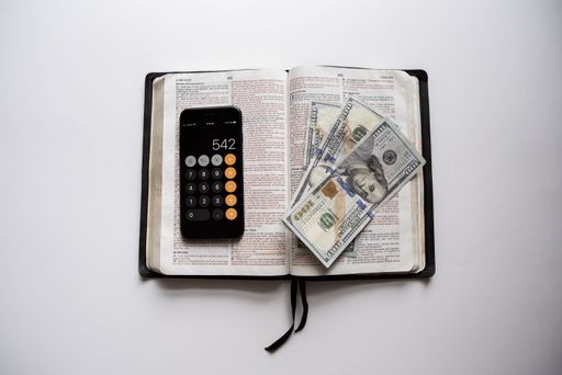 An overhead shot of an open book with hundred dollar bills and a smartphone on top