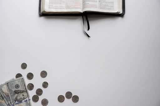 An overhead shot of an open bible on the top and hundred dollars Bills on the bottom on a white surface - concept money over religion