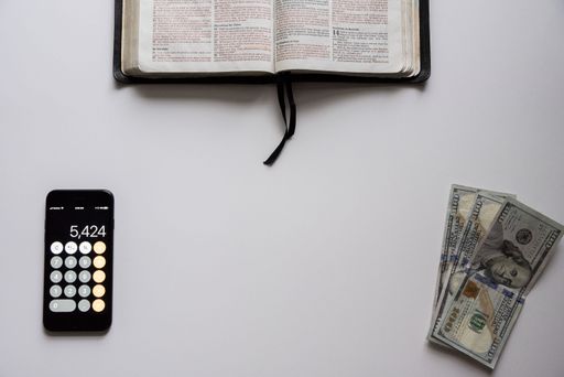 An overhead shot of an open bible with money and a smartphone on the bottom - concept money over religion