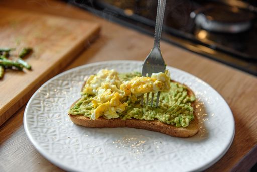 A close up of a hand taking avocado toast with scrambled eggs