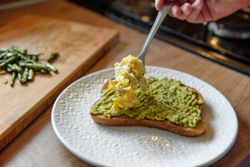 A close up of a hand taking avocado toast with scrambled eggs