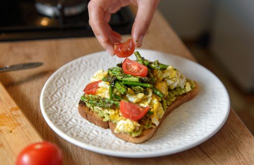 A Close up of a hand making avocado toast with eggs and cherry tomatoes