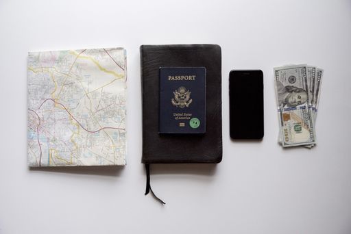 An overhead shot of a passport on top of a book in the middle of a smartphone, map, and bills - concept for traveling