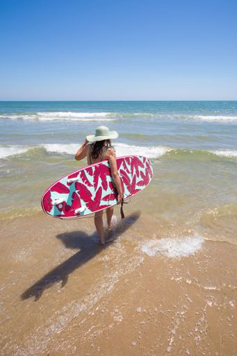 A Hispanic woman wearing swimwear while holding a surfboard on the beach