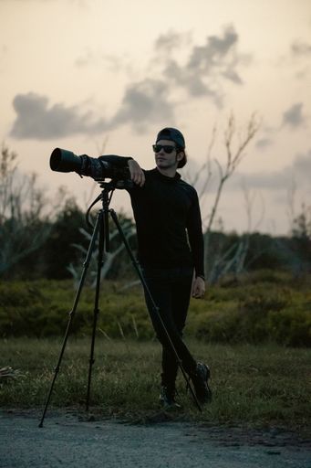 A cool male photographer posing with his camera on a tripod