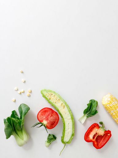 A top view of cut tomato, pepper, bitter gourd, corn and lettuce on white background
