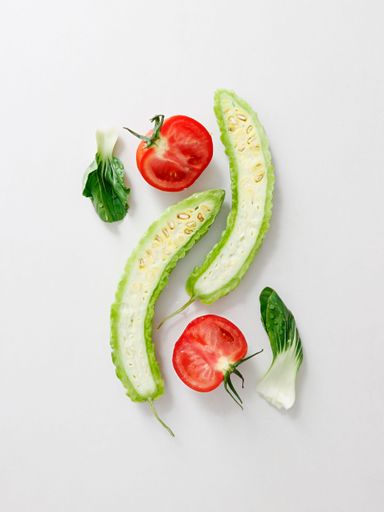 A top view of cut tomato, bitter gourd and lettuce on white background