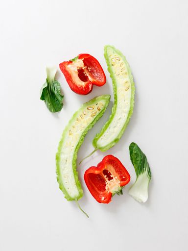 A top view of cut tomato, bitter gourd and lettuce on white background