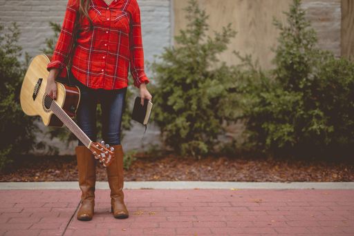 A beautiful shot of a female standing while holding a book and a guitar with a blurred background