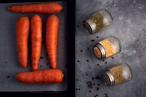 An overhead of carrots and herb jars on a gray kitchen table surface