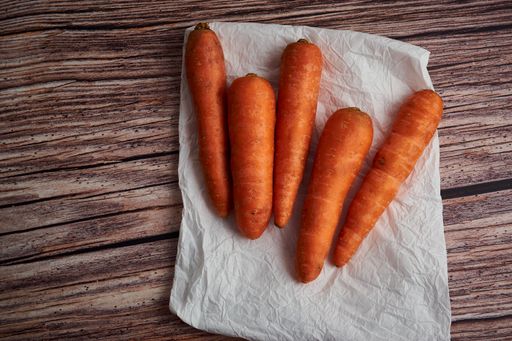 An overhead shot of carrots laying on a white kitchen cloth on a wooden surface