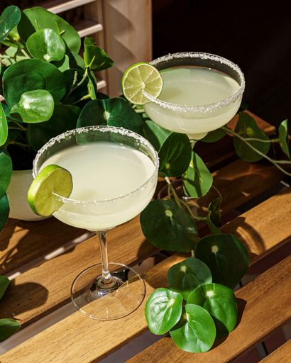 A vertical shot of two glasses of traditional lime margarita cocktails on a wooden table
