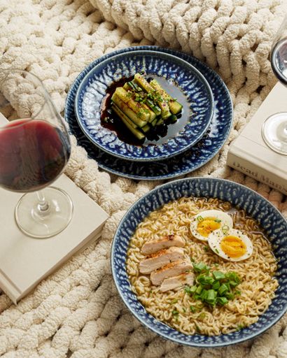 A vertical top view of miso ramen noodles with soy salted cucumbers and a glass of wine