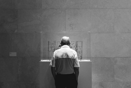 A grayscale of an old man appreciating a piece of art in the museum