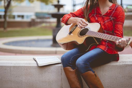 A female sitting beside a book while playing the guitar with a blurred background