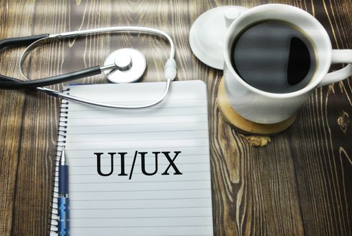A cup of coffee, phonendoscope, pen and notebook with UI UX inscription on a wooden table