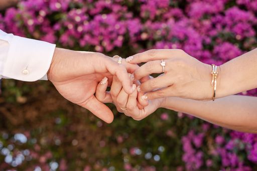 A Newly married couple holding hands and wedding rings in the foreground