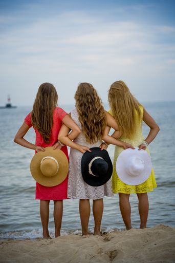 A beautiful shot of three female wearing different color dresses while holding hats behind their back