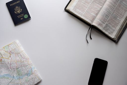 An overhead shot of a book, smartphone, passport and a map on a white surface - concept for traveling