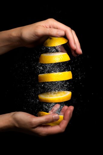 A vertical shot of two hands holding sliced lemons with the zest coming out on a black background - concept for a refreshing lemonade