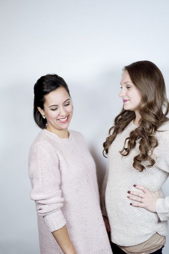 A vertical shot of to females standing near each other and smiling with a white background