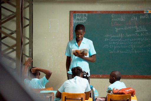 A young black boy reading in front of his classmates  at a school in Haiti