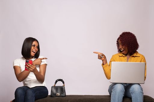 Two excited african females using phone and laptop for communication