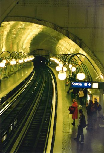 A vertical shot of the illuminated subway with people standing on the platform. Paris, France.