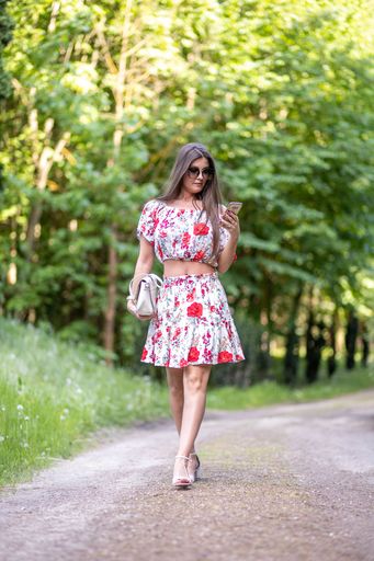 The vertical view of a female wearing a floral set walking in the park while looking at her phone