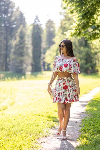 The vertical view of a woman wearing a floral set and sunglasses while walking in the park