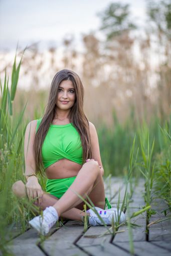 A young sexy Caucasian woman in a green top and shorts sitting on a wooden walkway and smiling
