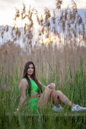 A young sexy Caucasian woman in a green top and shorts sitting on a wooden walkway against reeds