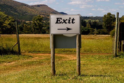 An eye-level shallow focus shot of an exit road sign in a field under the blue sky with clouds