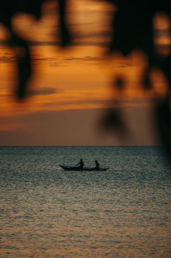 A vertical shot of two people on a boat sailing on the sea at sunset