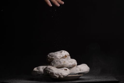 woman's hand pouring sugar into sugar doughnuts on black background
