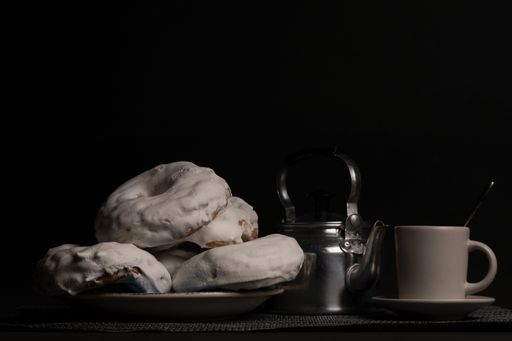 glazed sugar doughnut with coffee cup and metal teapot on black background