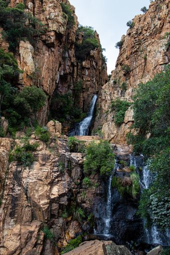 A vertical shot of a waterfall in a forest cascading down the cliffs