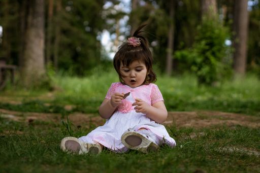 A close up of a little 2 year old girl in a park near a forest