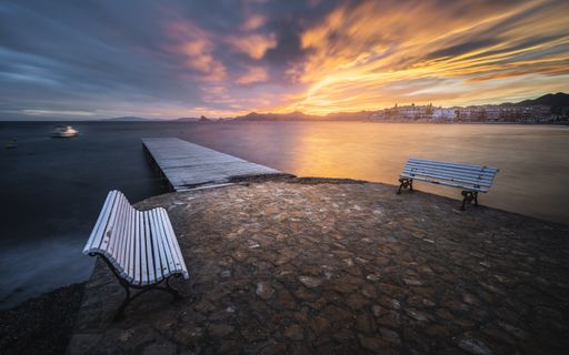 A mesmerizing seascape with a wooden pier and benches on the foreground at the scenic sunset
