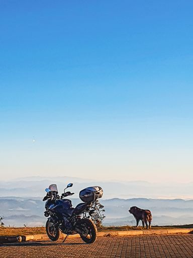 A vertical shot of a motorcycle with scenic mountains and skyscape in the background