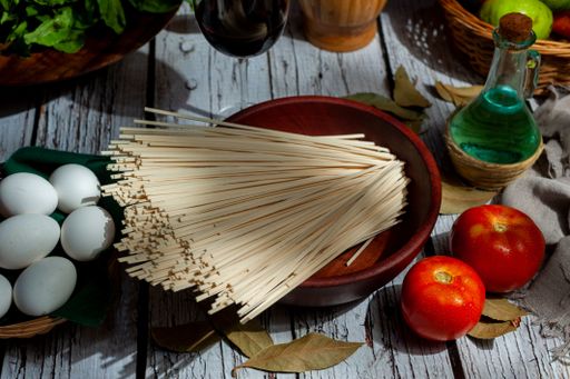 A high angle shot of of raw food ingredients on wooden table, spaghetti in a bowl, tomatoes and eggs