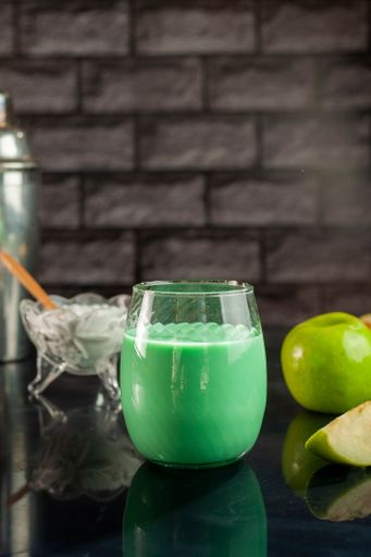 A vertical shot of a green apple smoothie juice on a black table and apples in the background