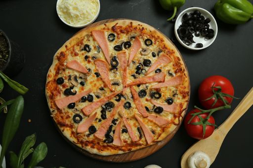 A top view of a sliced pizza with olives on a black background and fresh vegetables