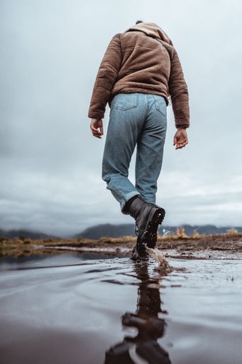A low angle shot of a Caucasian guy seen from behind, walking in a puddle in Northern Norway