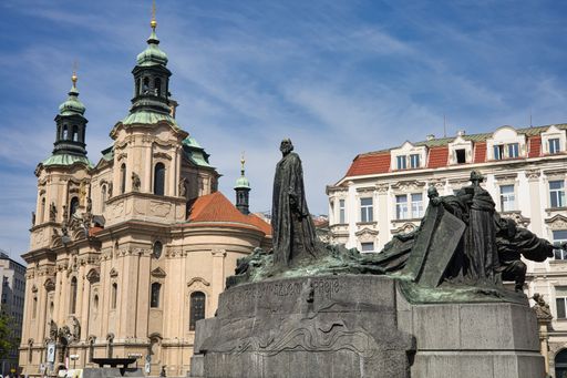 A view of castle behind Jan Hus memorial under blue bright sky in Prague