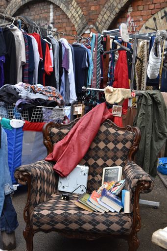 A vertical shot of an old chair with books and clothes in the background in Flea market, London