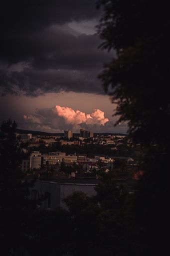 A dark sky at sunset with dramatic clouds and lighting behind a city skyline