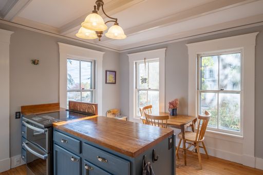A nicely decorated kitchen with big windows and a chandelier hanging from the ceiling